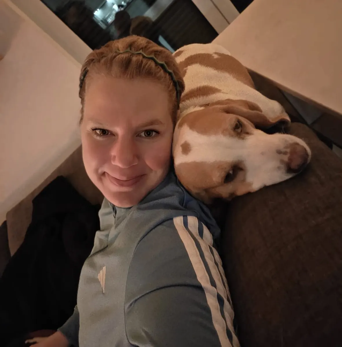Jana kuschelt mit einem Hund auf dem Sofa